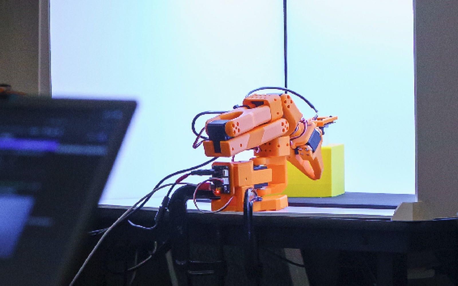 The physical robot arm on the lab desk beside the monitor running the simulator it is matched against.